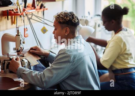 Side view of two women using sewing machines in leatherworking manufactory Stock Photo
