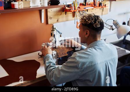 Back view of artisan using sewing machine in leatherworking shop, copy space Stock Photo