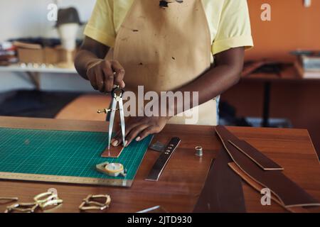 Close up of black female artisan cutting and measuring leather using traditional tools, copy space Stock Photo