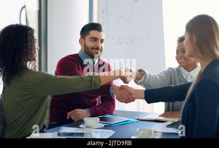 Merging together to realise their vision as a team. a group of young entrepreneurs shaking hands during an office meeting. Stock Photo