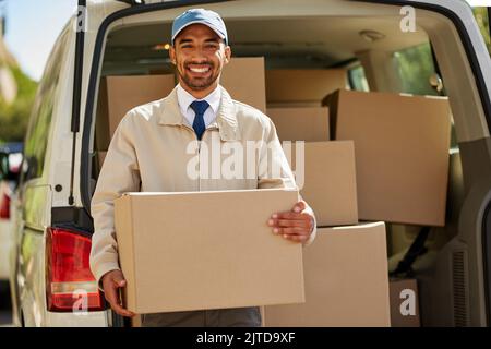 You order it, we deliver it. Portrait of a friendly delivery man unloading cardboard boxes from his van. Stock Photo