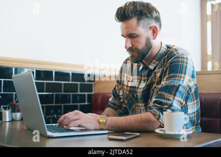 Sometimes, all you need is a change of scene. a young man using his laptop while sitting in a cafe. Stock Photo
