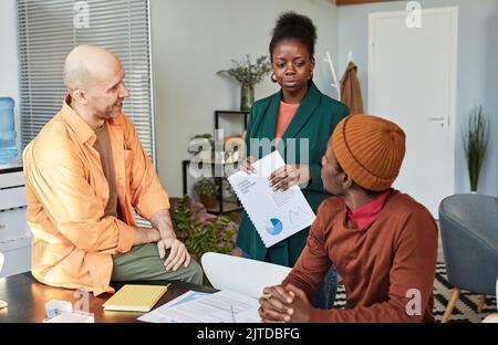 Portrait of successful black businesswoman talking to two colleagues in office while managing project Stock Photo