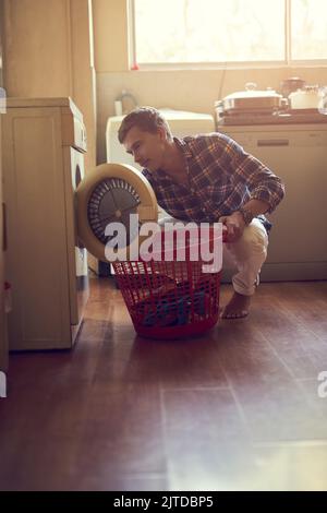 Mastering the art of laundry. a young man doing laundry at home. Stock Photo