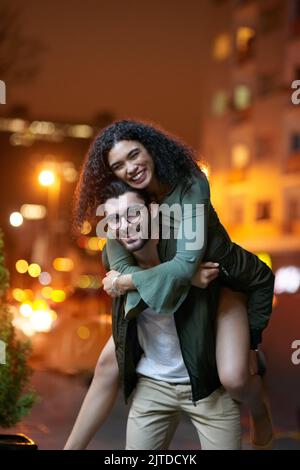 Love lifts you up. Portrait of a handsome young man piggybacking his girlfriend outdoors at night. Stock Photo