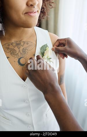 Hands of black man putting buttonhole flower on white elegant waistcoat of African American bride standing in front of him Stock Photo