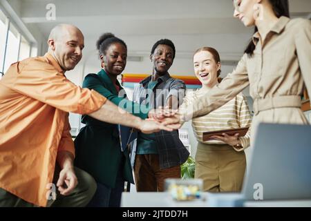Low angle view at diverse business team huddling in office and stacking hands with motivation Stock Photo