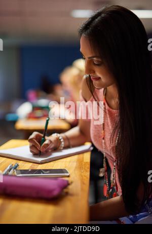 Pretty and diligent student making notes in notepad or copybook with ...