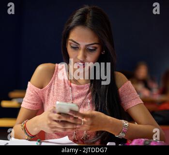 Help, Im in the wrong class. a university student using her cellphone while sitting in a lecture hall. Stock Photo