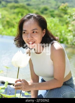 Vietnamese young woman smiling and smelling a white lotus in Vietnam Stock Photo