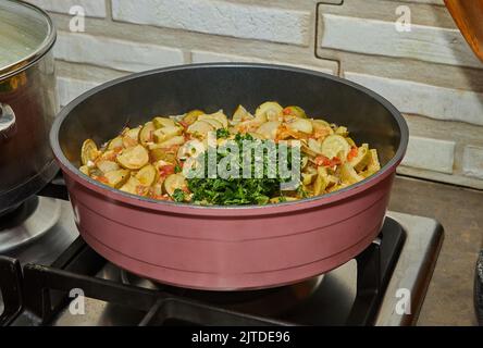 Zucchini with carrots and parsley are fried in pan on gas stove Stock Photo