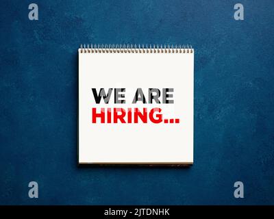 The message we are hiring on a notebook on blue business office desktop. Job employment concept. Stock Photo