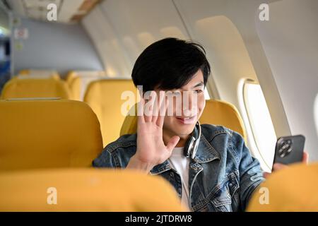 Happy and cheerful young Asian male traveler passenger video calling with his girlfriend after landing at his destination. Airplane journey concept Stock Photo