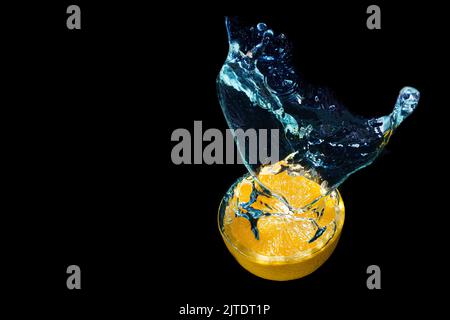 Fresh halved citrus fruit dropped in water with splashes on black background Stock Photo