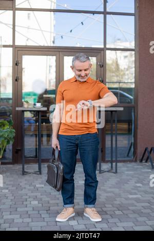 Gray haired gentleman focused on staking young tomato plants, merging ...