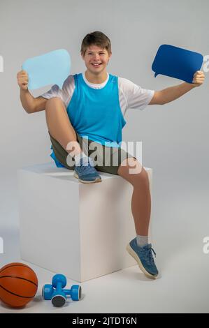 A smiling boy sitting on a cube with comments signs in hands Stock Photo