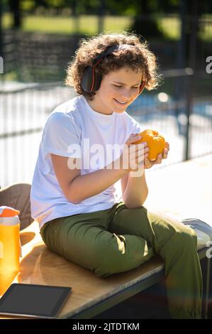 Pleased teen with an orange sitting in a street cafe Stock Photo