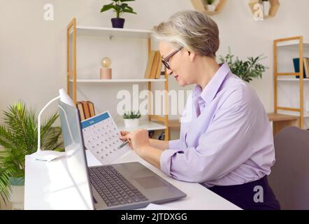 Senior successful business woman planning her work week and checking paper calendar. Stock Photo