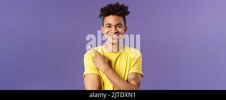 Close-up portrait of enthusiastic, happy young hipster male with dreads, beaming smile and pointing finger upper left corner, present cool product Stock Photo