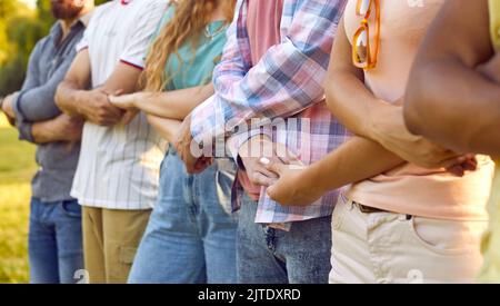 Multiracial people men and woman hold hands as sign of friendship or unity stand in row in park Stock Photo