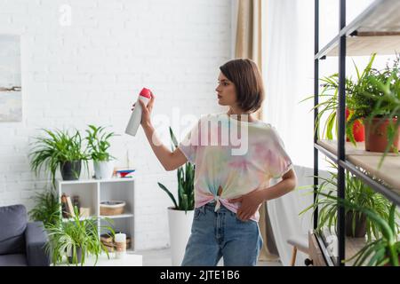 Young woman spraying air freshener while standing in living room Stock Photo