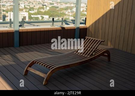 Wooden sun lounger on the roof of the penthouse overlooking the city. Soft selective focus. Stock Photo