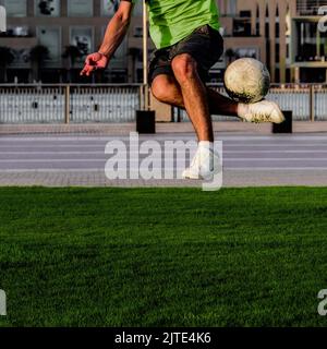 unrecognizable white skinned colored man in a green soccer sports uniform holding up a soccer ball while doing skilled tricks on a urban field Stock Photo