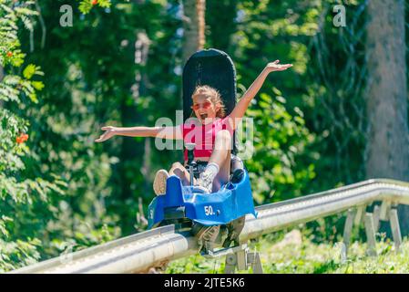 Screaming girl riding mountain roller coaster with outstretched arms. Forest in background Stock Photo