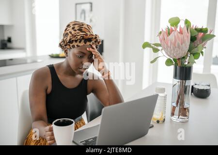 Young Black African woman tired, exhausted from working studying hard from home. Bored and frustrated looking at laptop. Head resting on hand. Stress Stock Photo