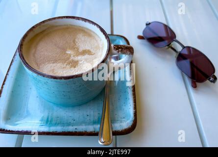 Cappuccino coffee in modern blue cup and saucer with a pair of sunglasses Stock Photo