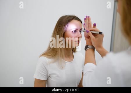 Doctor neurologist shining flashlight on patient eyes to see pupil reaction to light in clinic Stock Photo