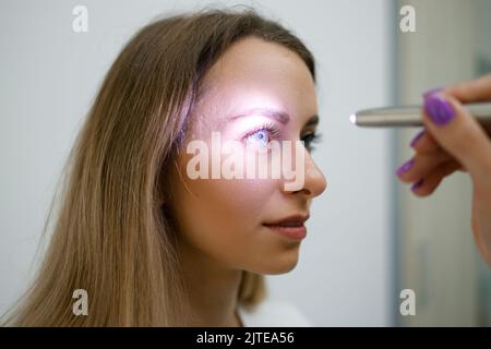 Close up view of doctor testing reflexes of the eye of young woman using a flashlight in medical clinic. Neurological physical examination Stock Photo