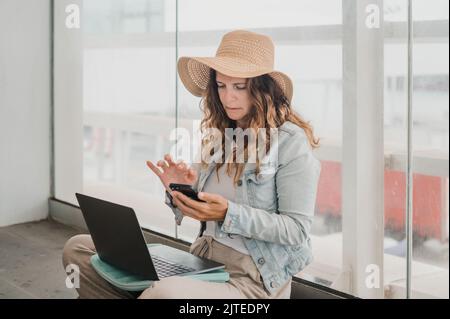 Freelancer with laptop using smartphone near window Stock Photo