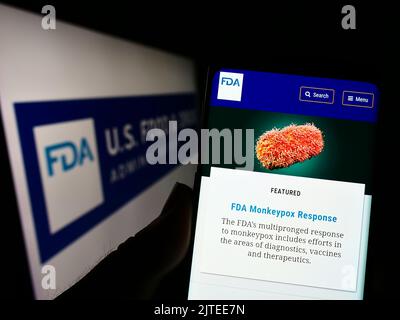 Person holding cellphone with website of United States Food and Drug Administration (FDA) on screen with logo. Focus on center of phone display. Stock Photo