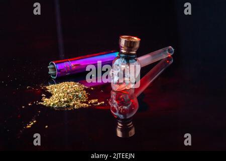 Cool glass smoking pipe in the shape of skull and pile of weed. Cannabis marijuana use concept. Stock Photo