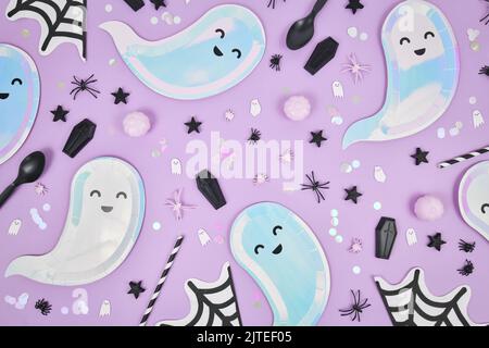 Cute pastel colored Halloween party flat lay with ghost shaped plates, spider web napkins and confetti on violet background Stock Photo