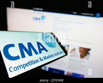 Smartphone with logo of British Competition and Markets Authority (CMA) on screen in front of website. Focus on center-left of phone display. Stock Photo