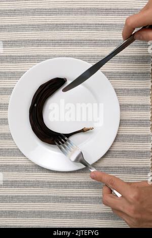 Man with fork and knife is preparing to eat black moldy dried banana on white plate. Not enough food in hungry time. Stock Photo