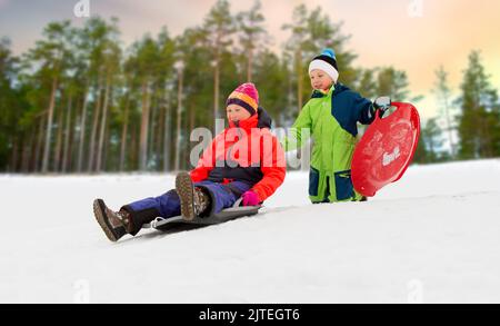 children sliding on sleds down snow hill in winter Stock Photo