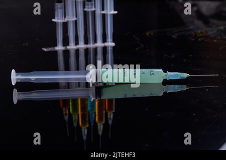 Close-up syringed fully filled with some green liquid medicine. Black reflective surface. Stock Photo