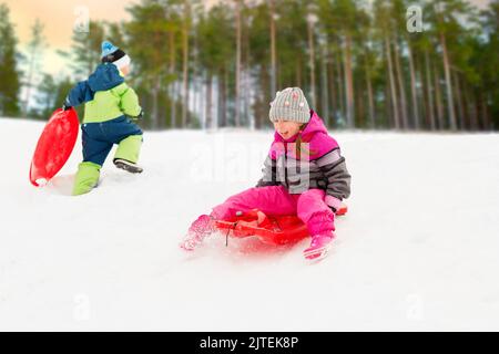 children sliding on sleds down hill in winter Stock Photo