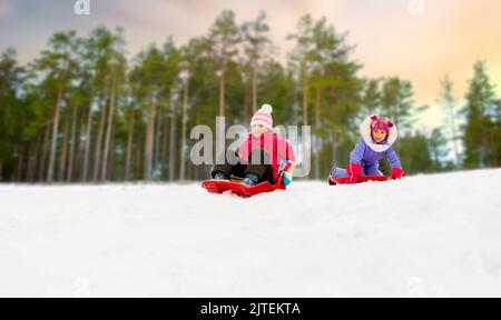 girls sliding on sleds down snow hill in winter Stock Photo