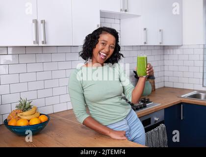 A happy young woman poses with fresh green smoothie in modern kitchen Stock Photo