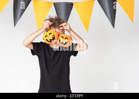Children's Halloween. A beautiful emotional boy in a black T-shirt holds Jack's lantern on a white studio background decorated with a black and orange Stock Photo
