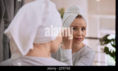 A Caucasian woman with a towel wrapped on head tweezing eyebrows Stock Photo