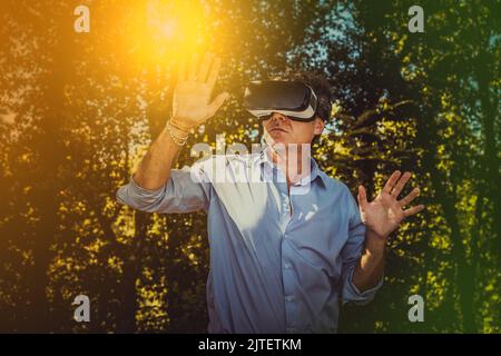 Young man is using a virtual reality headset in the park. Beautiful businessman is working with a viewer outdoors. Stock Photo