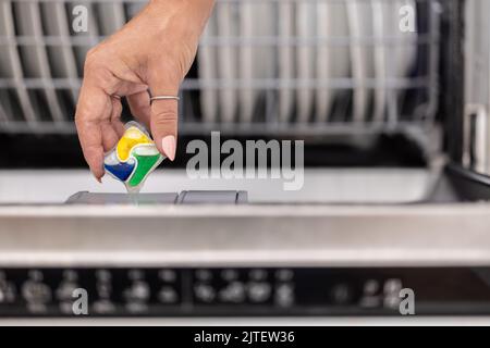 Detail of a female hand putting colorful detergent tablet into the dishwasher. Stock Photo