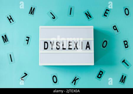 White lightbox with DYSLEXIA word and different letters haphazardly scattered on light blue background. Top view Stock Photo