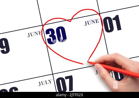 30th day of June. A woman's hand drawing a red heart shape on the calendar date of 30 June. Heart as a symbol of love. Summer month. Day of the year c Stock Photo