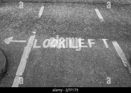 A gray road in Dublin, Ireland with a painted sign that says 'Look Left' with a white arrow. Stock Photo